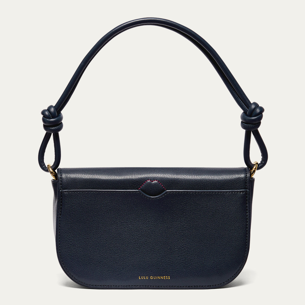 Navy leather shoulder bag with knotted handle and showing the back slip pocket and red stitched lip detail on a light grey background