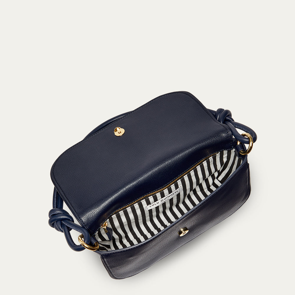 Navy blue leather shoulder bag with gold accents open revealing a black and white striped lining on a light gray background