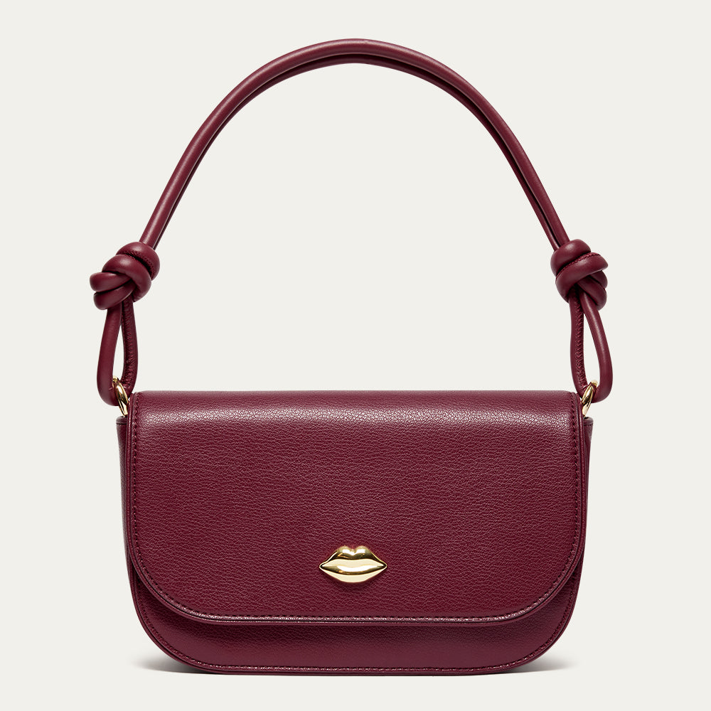 Burgundy leather shoulder bag with gold lip detail and a knotted shoulder strap on a light grey background.