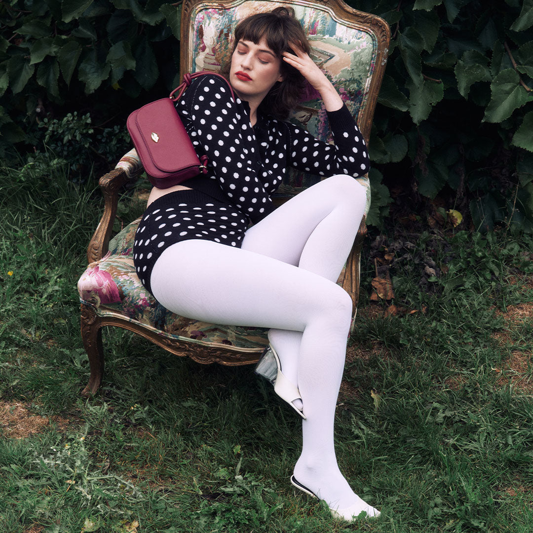 Woman in polka dot outfit sitting on a vintage chair outdoors with a burgundy leather bag on her shoulder