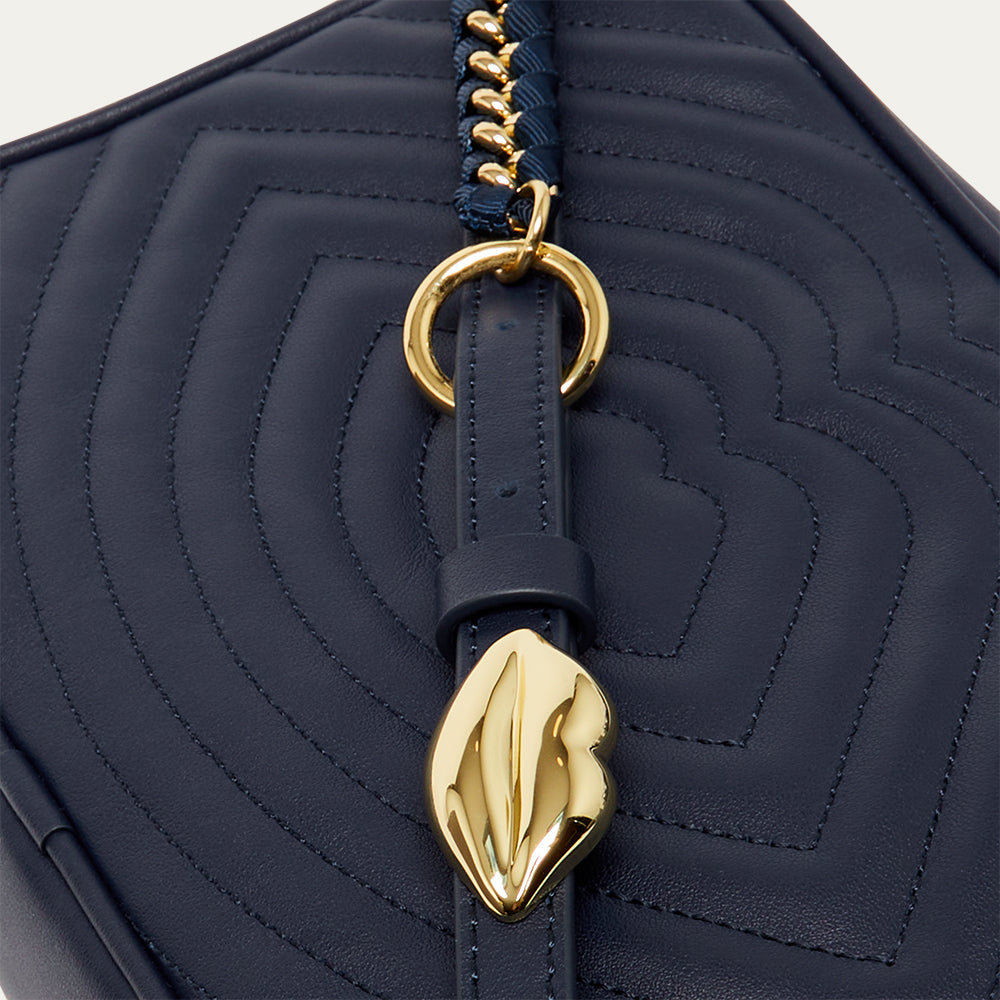 Navy blue quilted leather handbag with gold lip accents on a light gray background