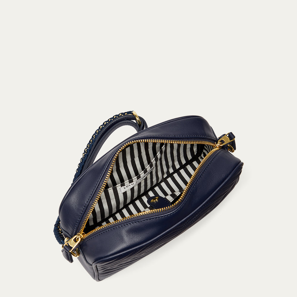 Inside image of a navy blue leather handbag with gold zipper revealing a black and white striped lining and inside pocket on a light gray background