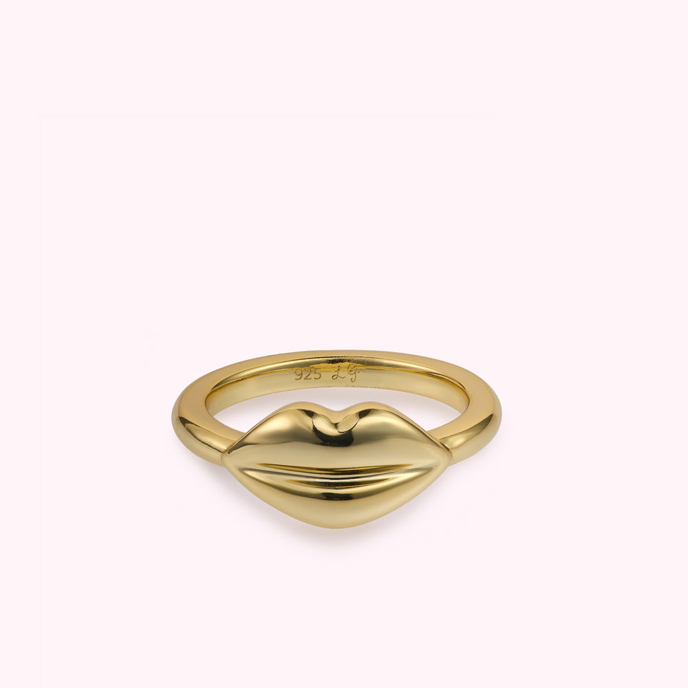 Front image of a gold lip shaped ring laying flat on a white background.