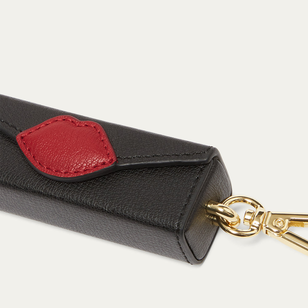 Black leather key charm with a red lip patch and gold keychain on a light gray background