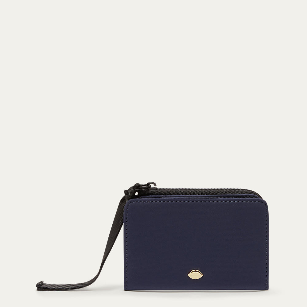 Navy blue wallet with a black ribbon zip pull on a light gray background