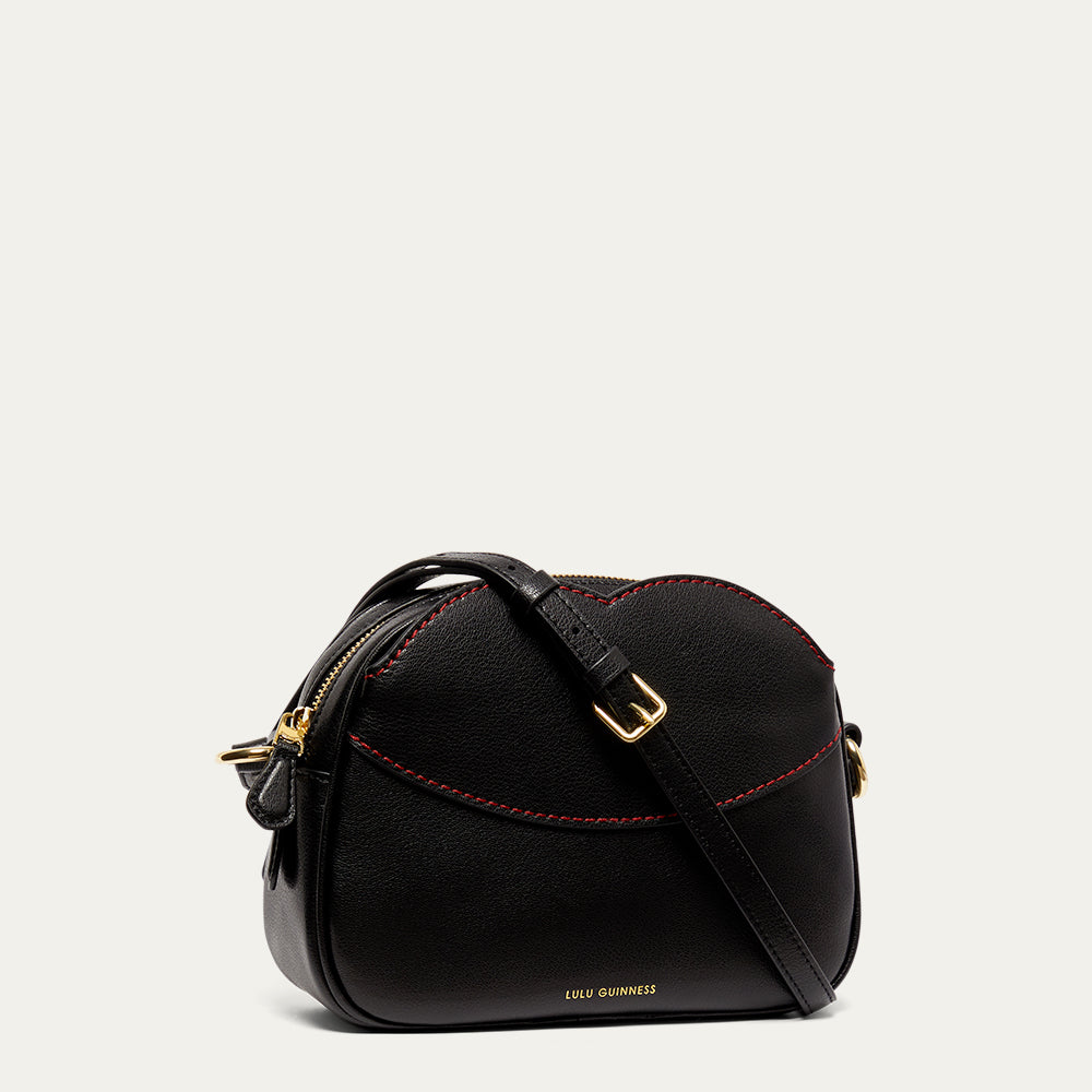 Black leather crossbody handbag with red stitching and gold accents on a light gray background