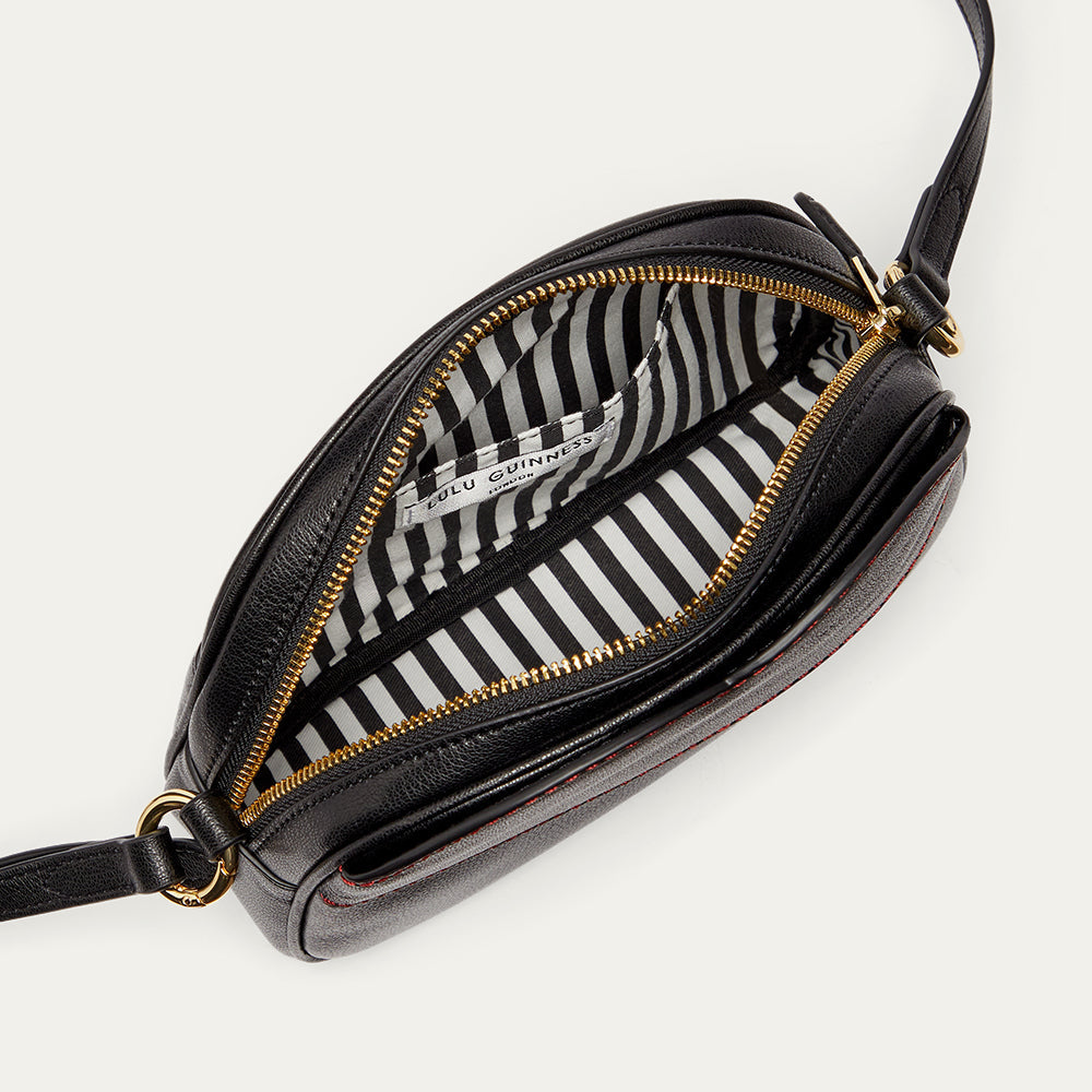 Inside image of a black leather crossbody bag revealing a black and white striped lining and inside pocket.