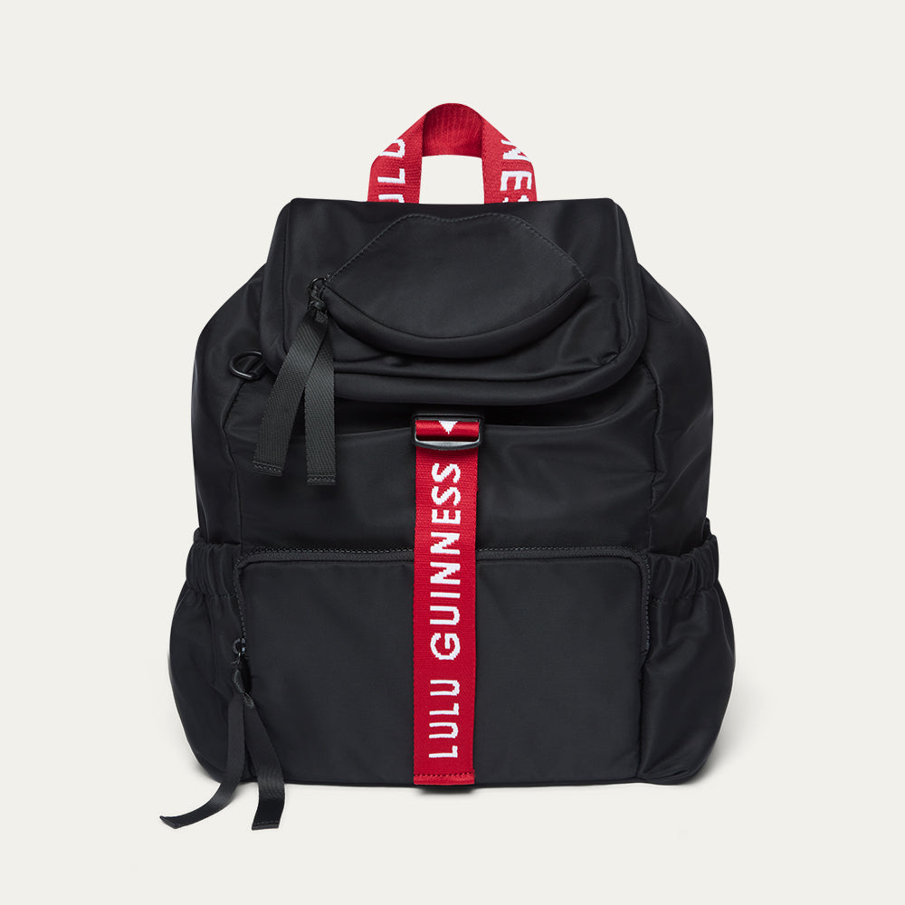 Black backpack with a red strap featuring 'Lulu Guinness' branding on a light gray background.