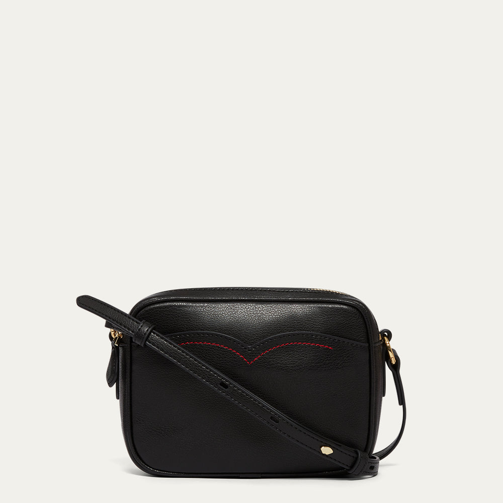 Black leather crossbody bag with red stitching on a light gray background