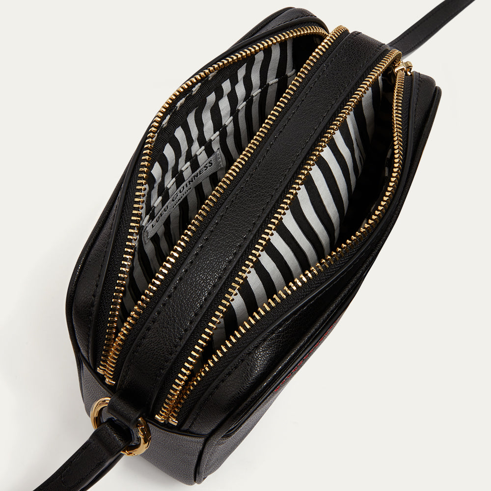 Open black handbag with gold zipper revealing a black and white striped lining on a white background