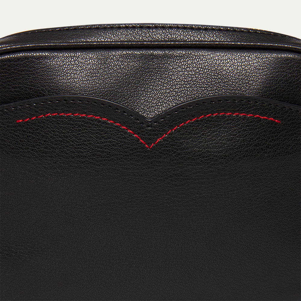 Close-up of black leather handbag with red stitching on a light gray background
