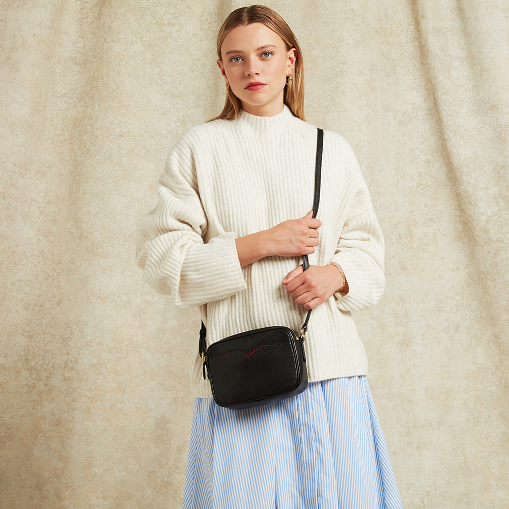 Woman holding a black handbag against a beige background