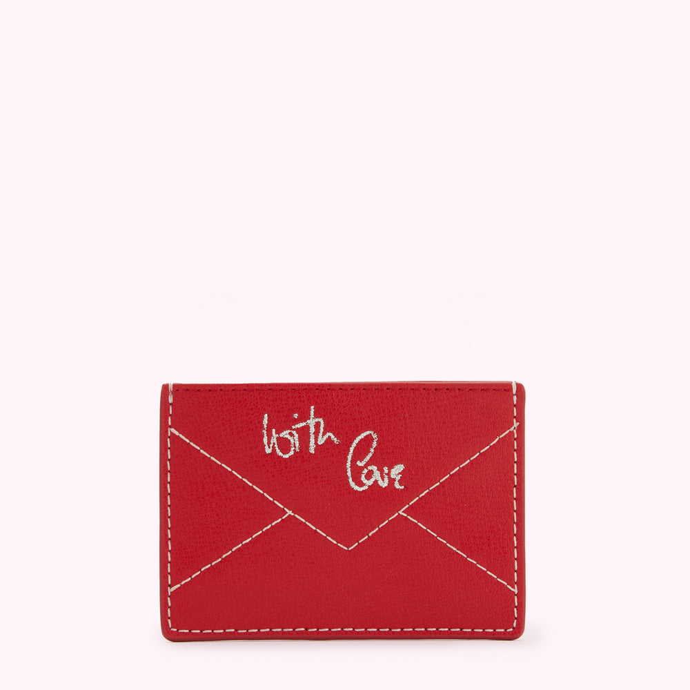 Red leather cardholder with "With Love" embroidered on the front in off-white thread, designed in the shape of an envelope.
