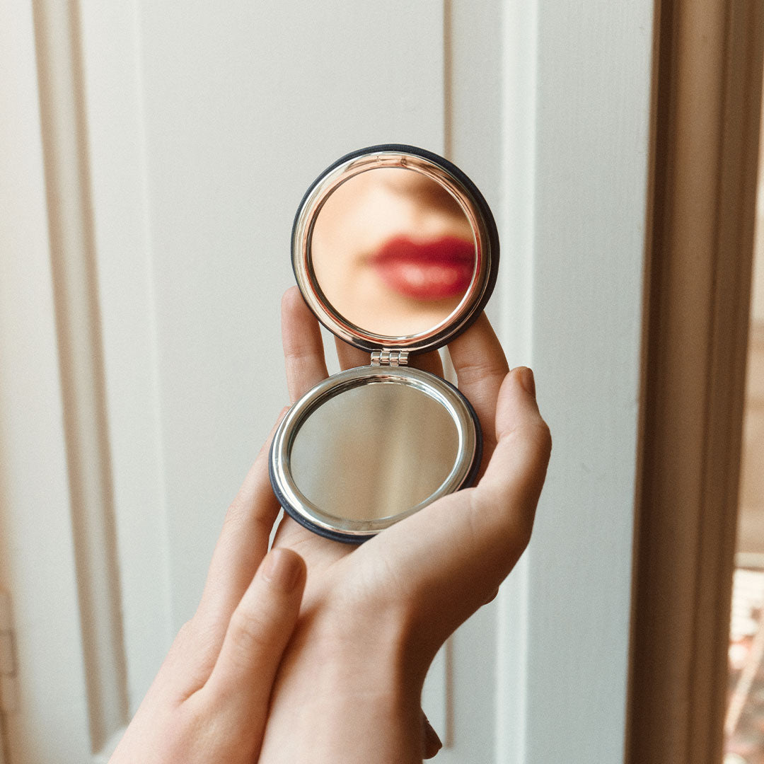 Hand holding a compact mirror with a blurred reflection against a neutral background