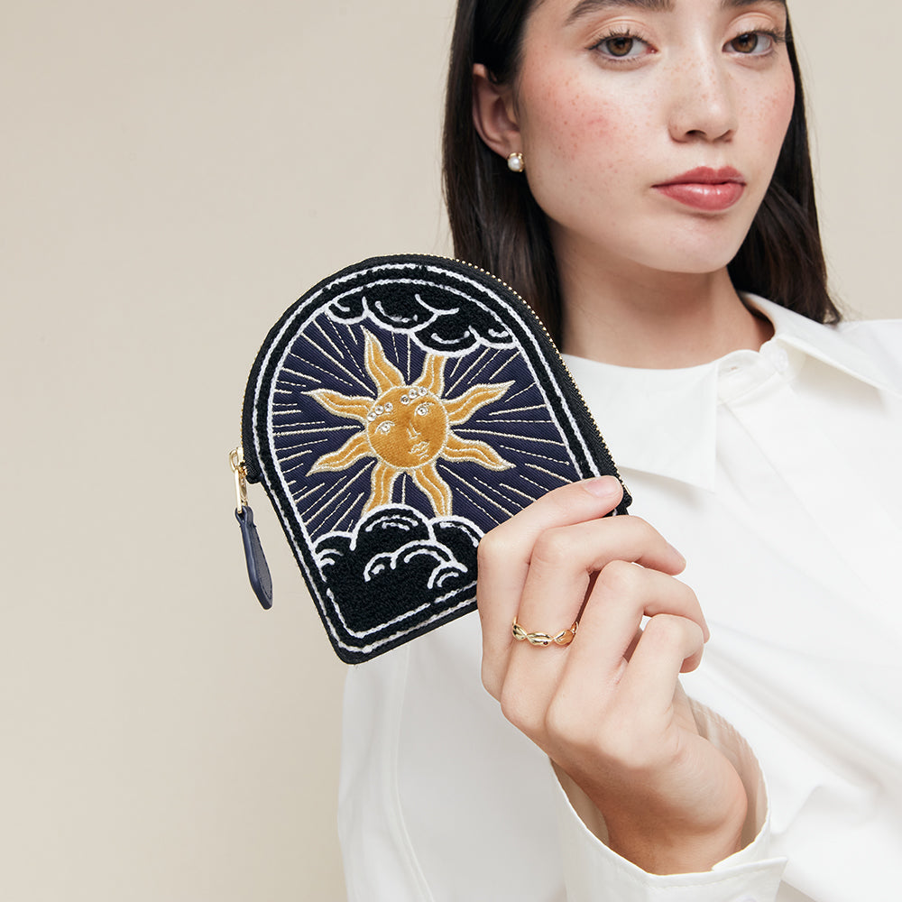 Woman holding a coin purse with a sun design against a beige background