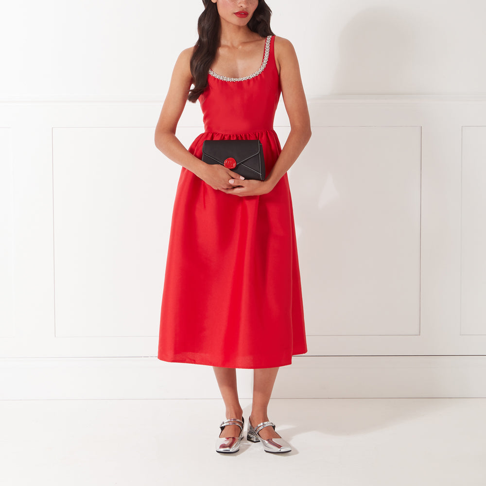 Woman in a red dress holding a black envelope clutch with a red wax seal.