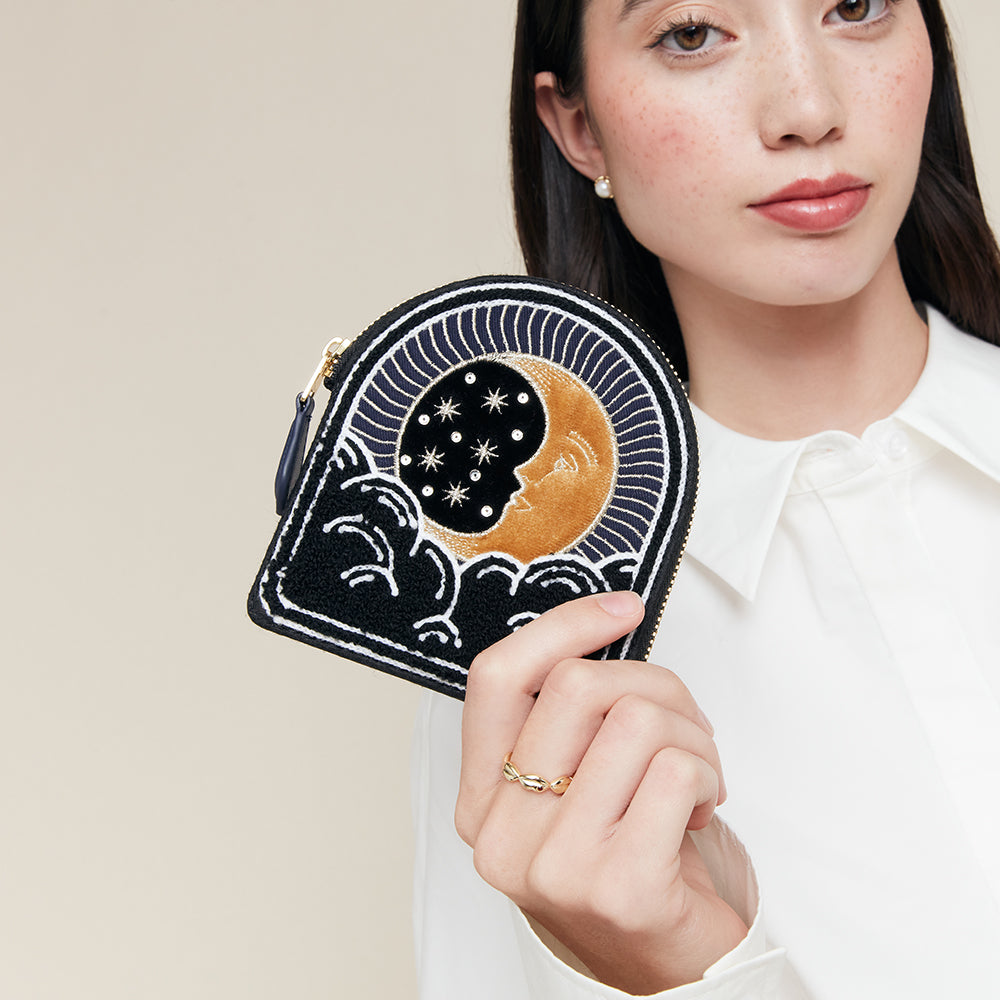 Woman holding a black, navy and gold moon. stars and clouds coin purse with celestial design