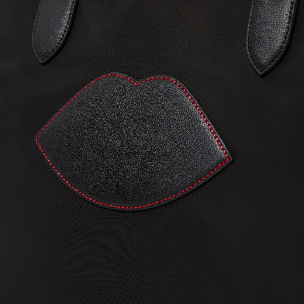 Black leather tote bag with red stitching shaped like lips on a black background