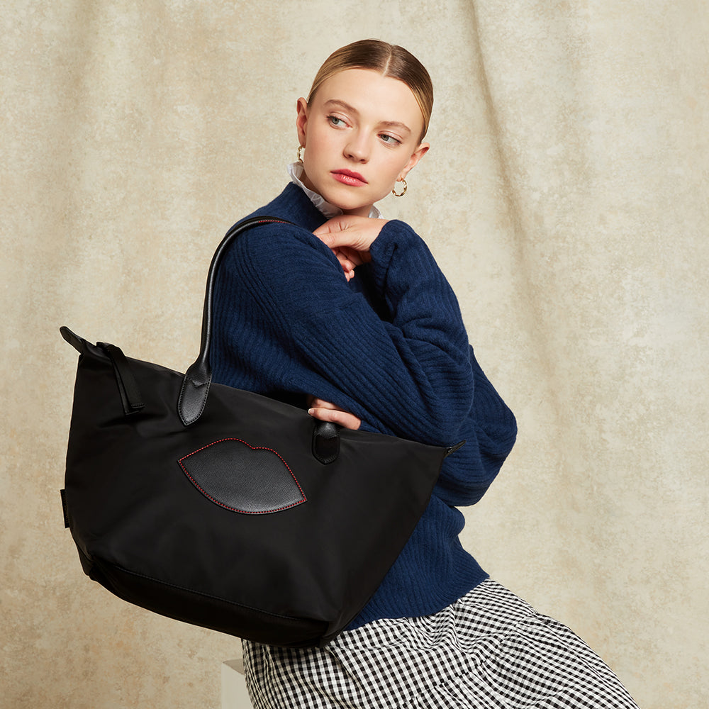 Woman holding a black tote bag with lip detail against a beige background
