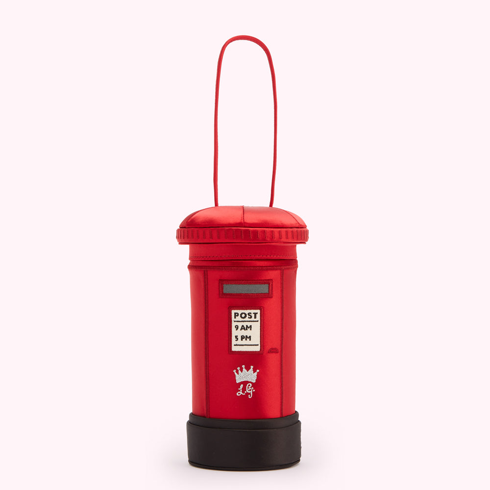 Red satin postbox-shaped handbag with black base and top, and a loop handle. The postbox features the words "POST", "9 AM", and "5 PM" along with a crown and initials.
