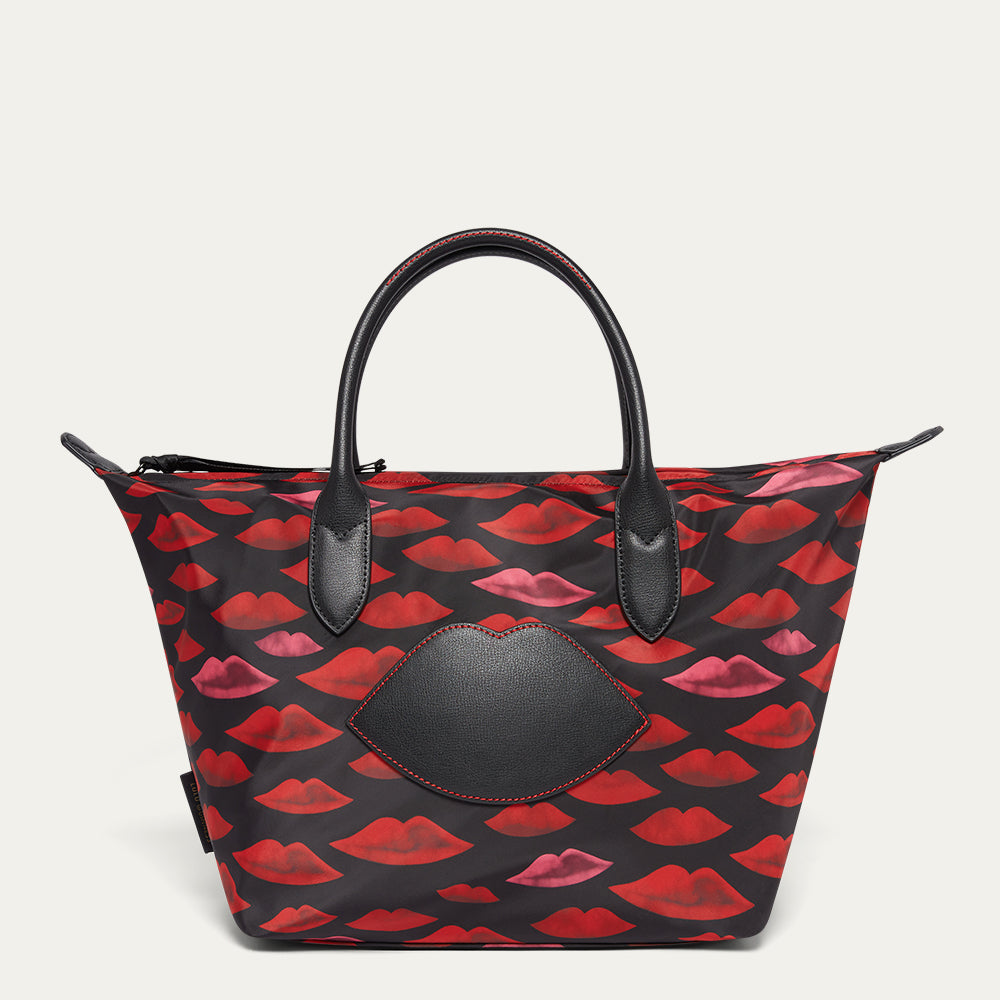 Tote bag with red and pink lip pattern and black leather lip patch on a beige background