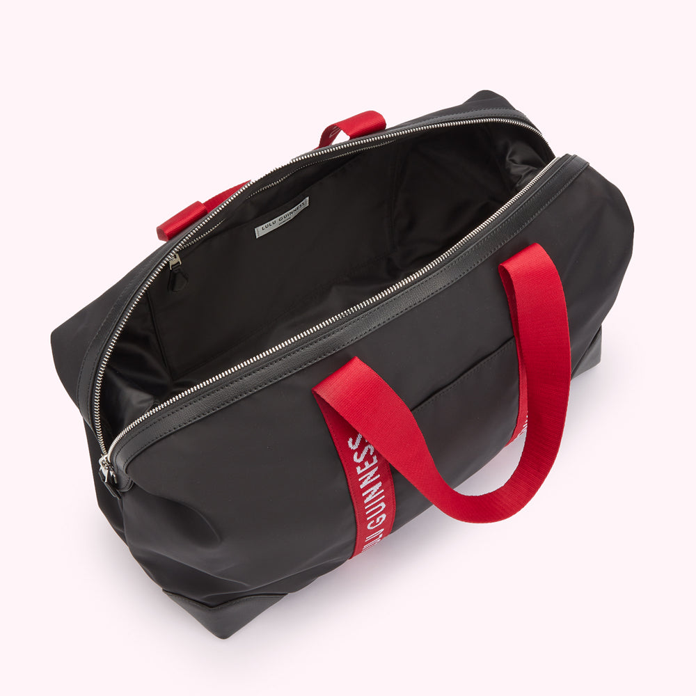 Inside image of a black nylon holdall duffle bag with red Lulu Guinnes sbranded straps revelaing a inside zip pocket.