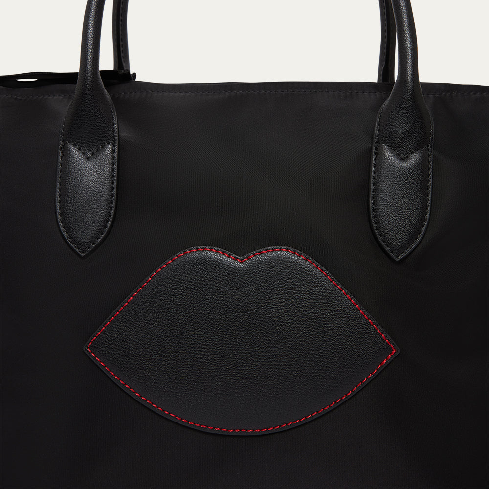 Black tote bag with a lip-shaped patch on a white background