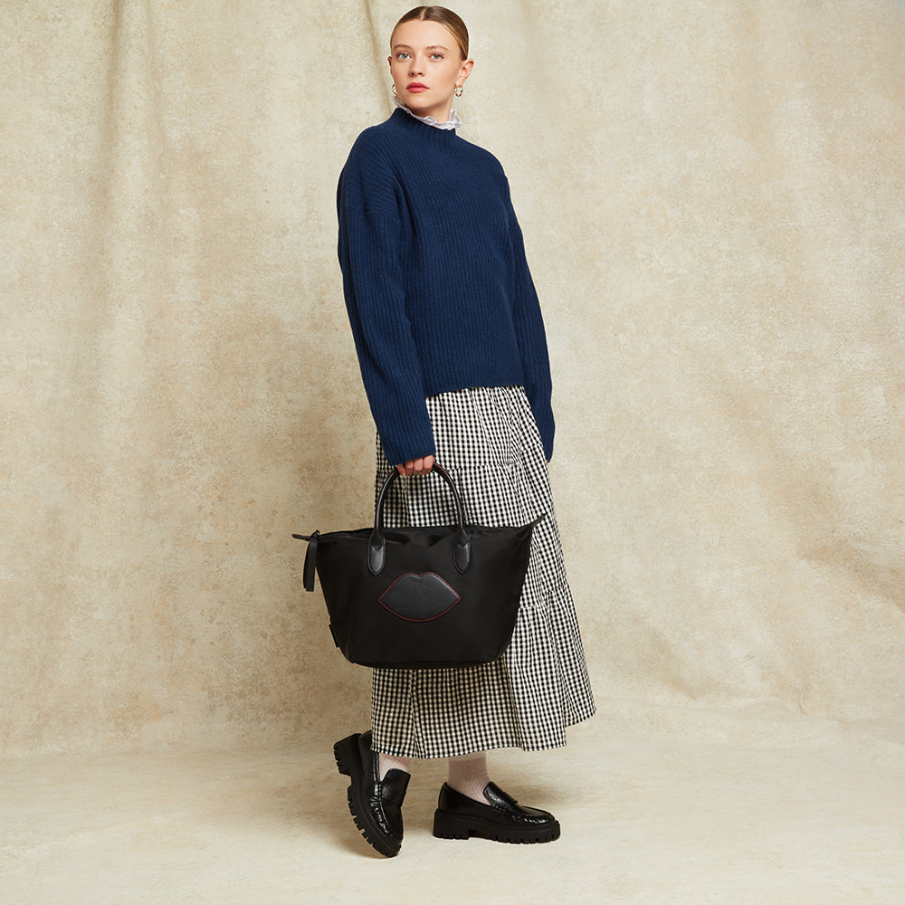 Woman holding a black handbag against a beige background