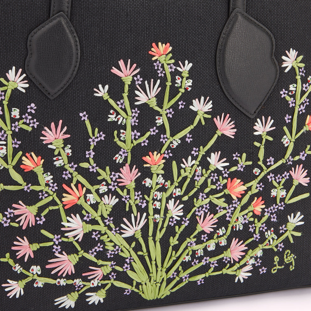 Close up image of pastel floral embroidery on a black canvas and leather tote bag with leather lip handle anchors.