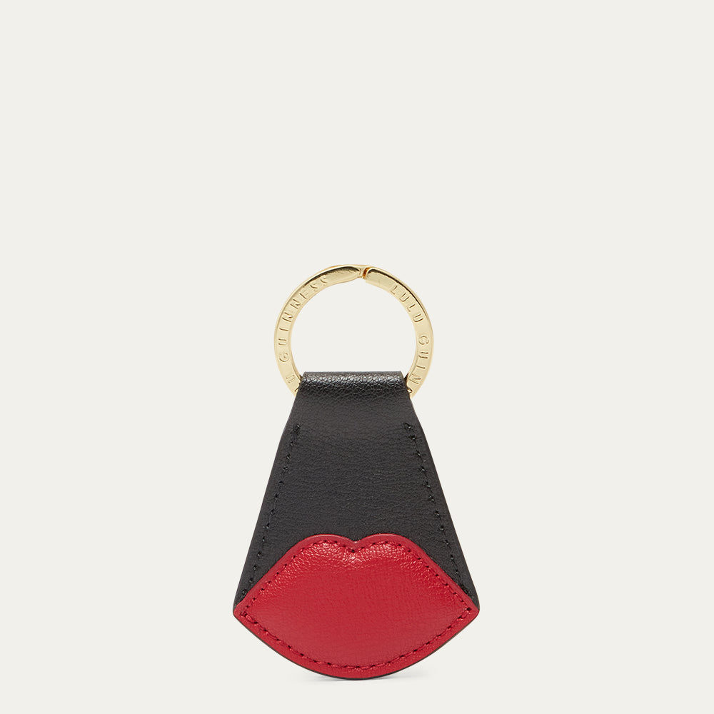 Black and red lip-shaped keychain with gold ring on a light gray background