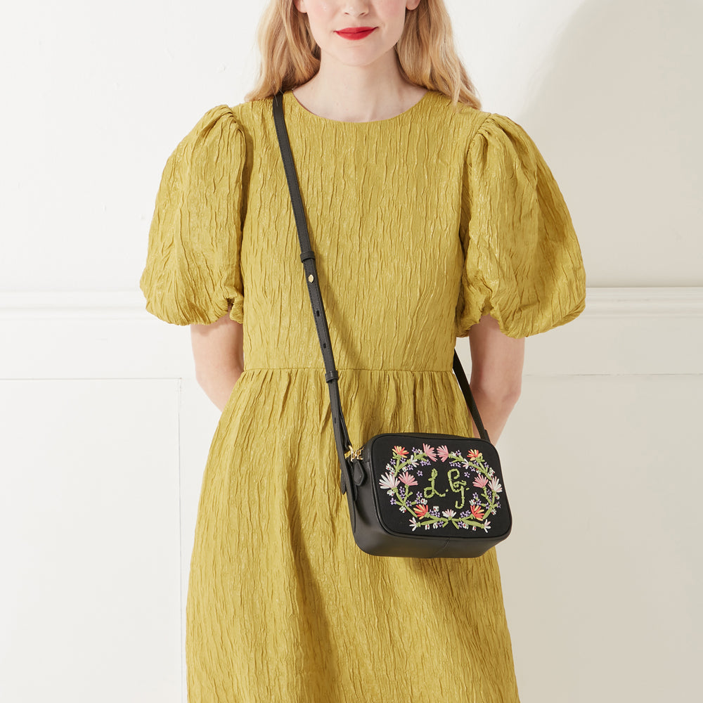 Model wearing a yellow dress wearing a black canvas and leather floral embroidered crossbody bag with embroidered L.G. monogram.