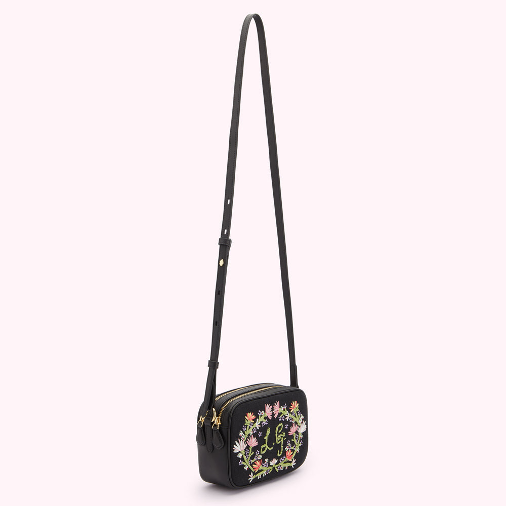 Black canvas and leather crossbody bag with hanging on a white background. Bag has pastel floral embroidey on the front with a embriodered L.G monogram.