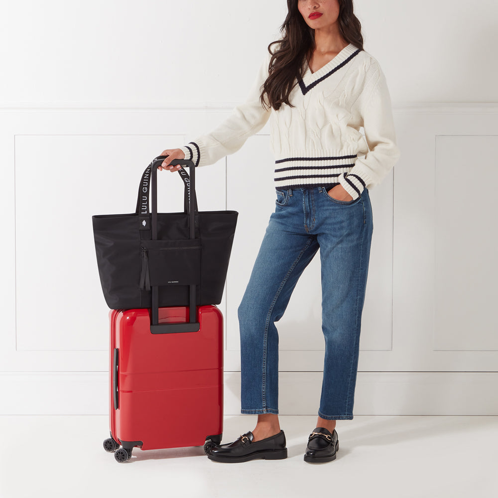 Model standing next to a suitcase with a black nylon tote bag slotted over the suitcase handles.