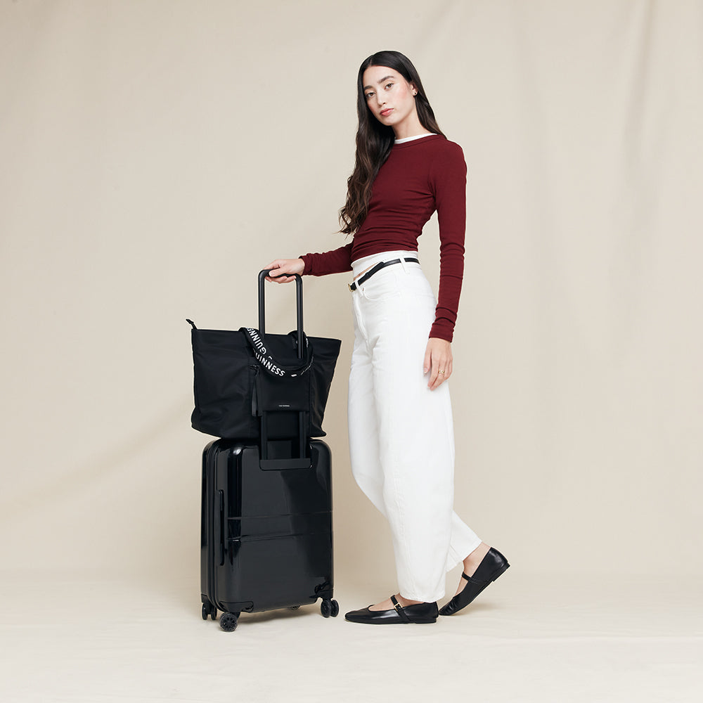 Woman holding a black suitcase and tote bag on a beige background