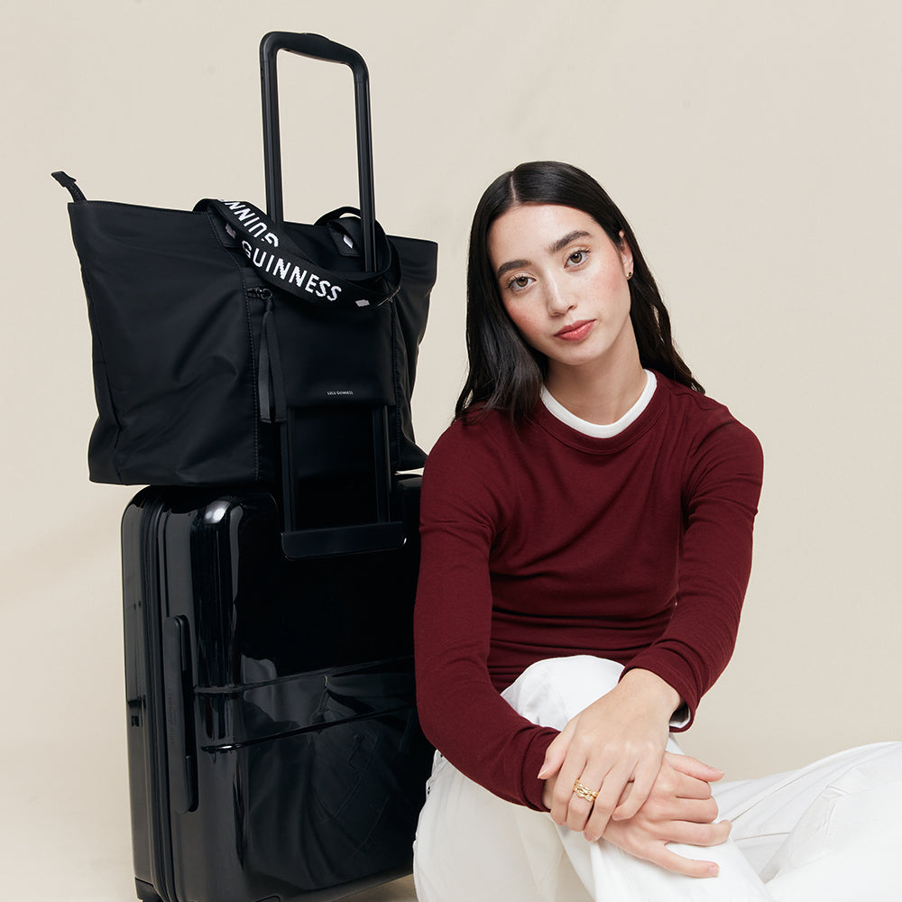 Woman sitting next to a black suitcase and bag with visible branding.