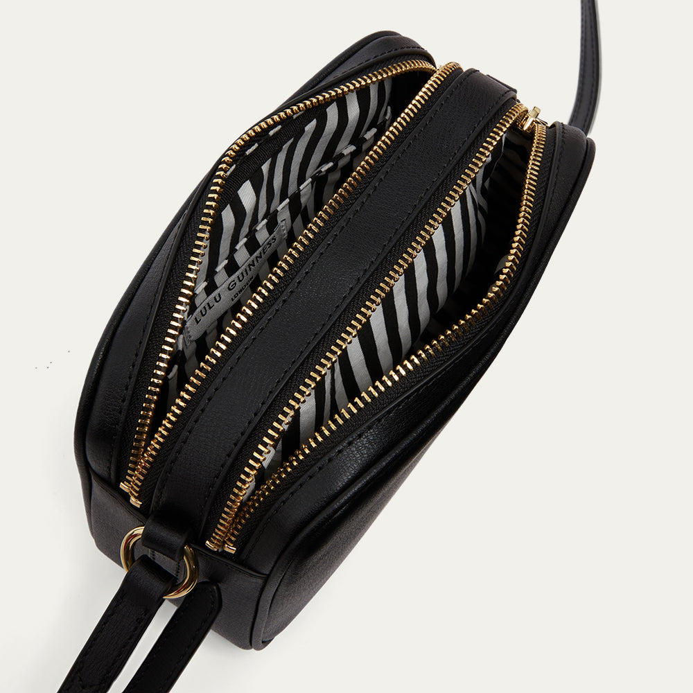 Black handbag with gold zippers open to reveal a black and white striped lining on a light gray background
