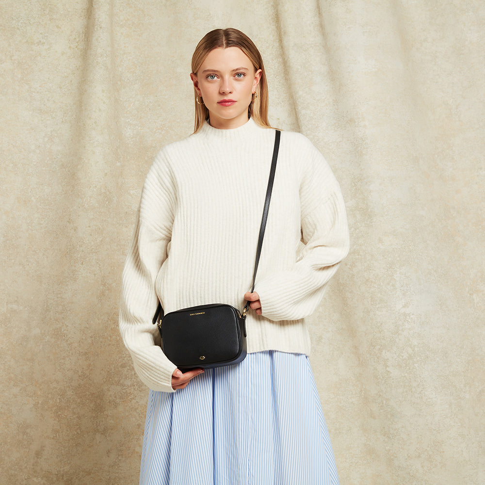 Woman holding a black crossbody bag against a beige background