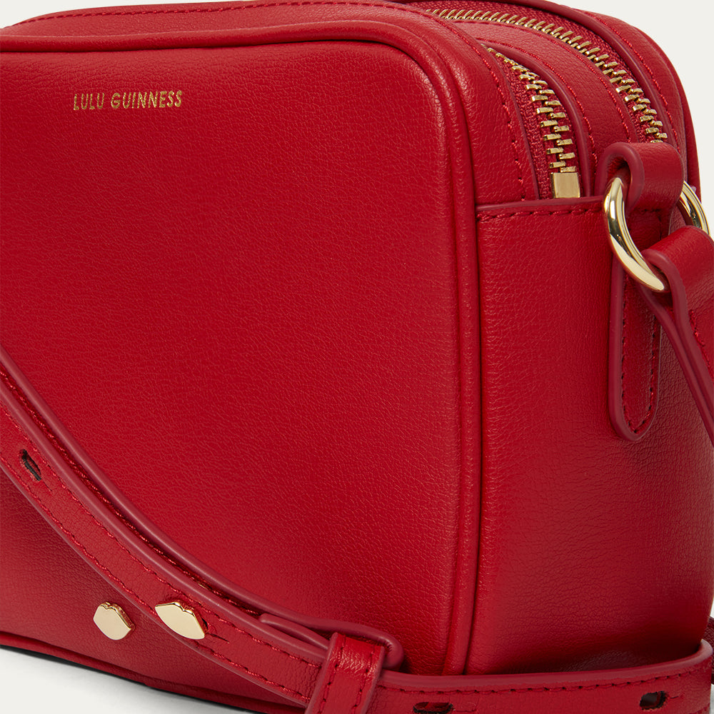 Red handbag with gold accents and 'Lulu Guinness' branding on a light gray background