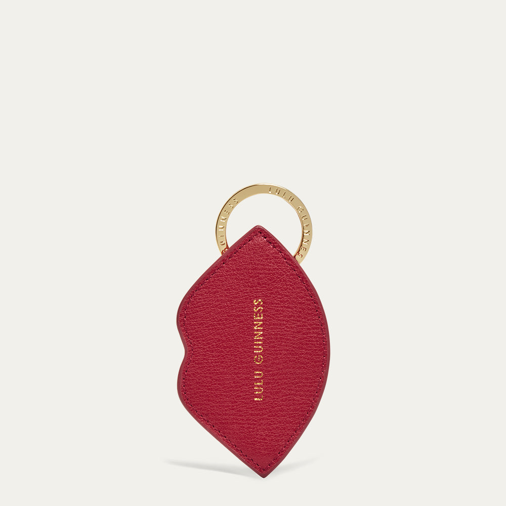 Red lip shape keychain with gold ring and gold printed 'Lulu Guinness' logo on a light grey background