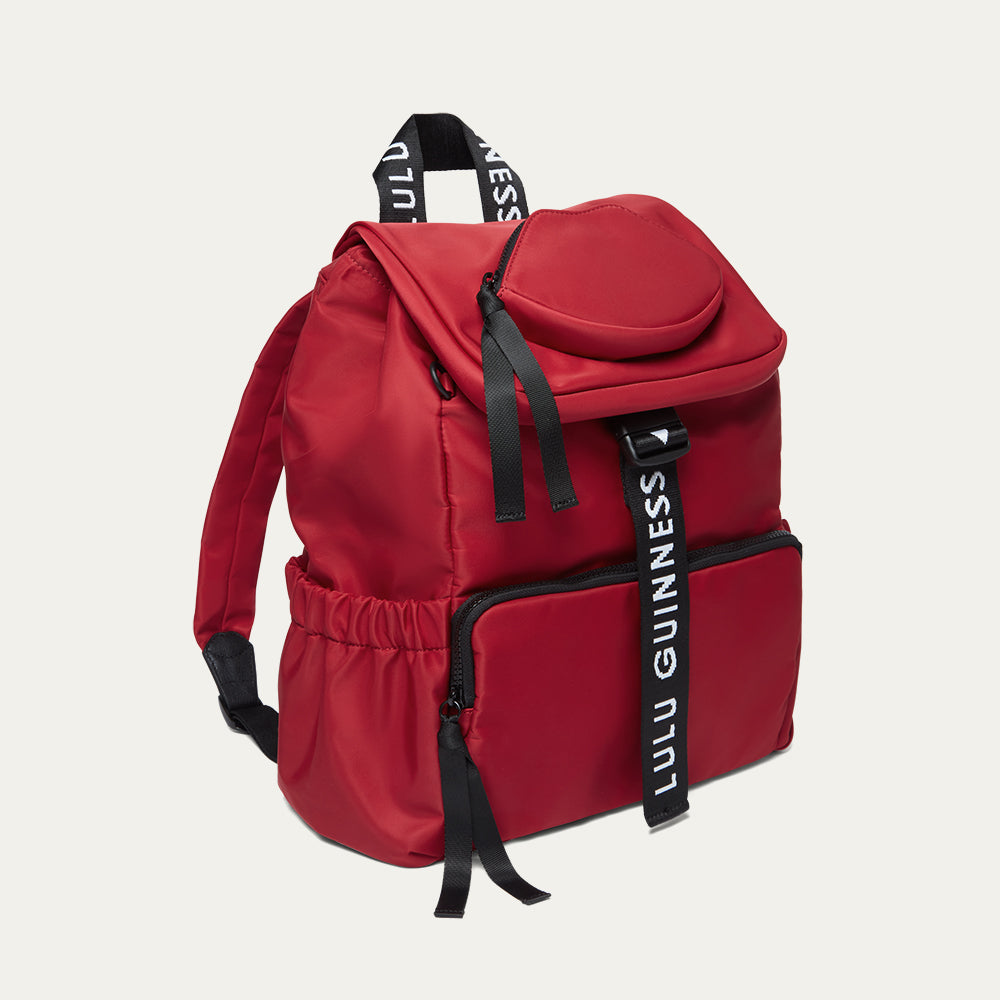 Red backpack with black straps and 'Lulu Guinness' branding on a light gray background