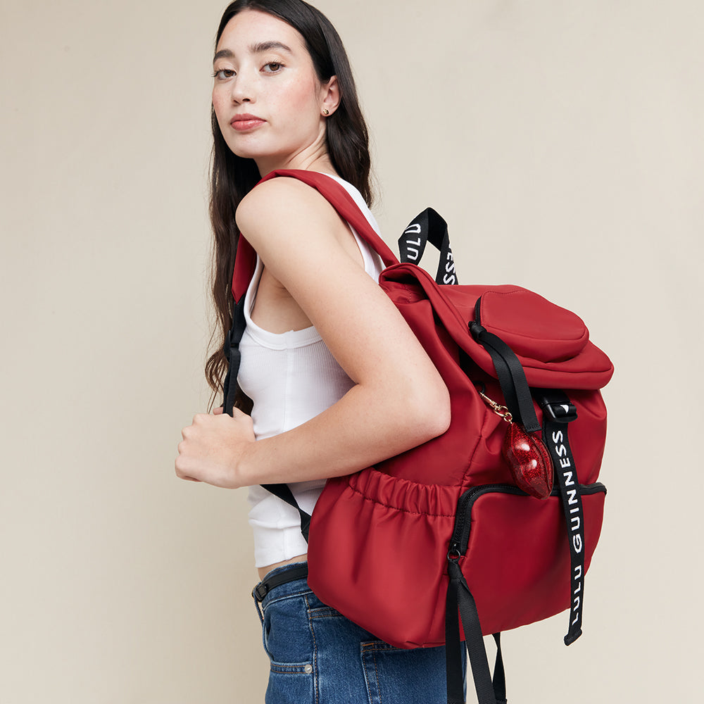 Woman wearing a red backpack with visible 'Lulu Guinness' branding on a beige background