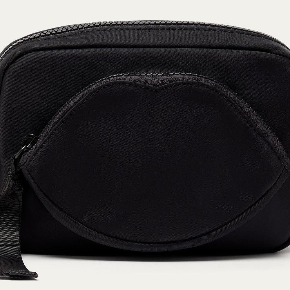 Close up image of a black crossbody bag with a lip-shaped pocket on a light gray background