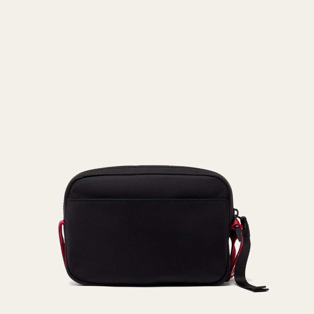 Black crossbody bag with red accents on a light gray background