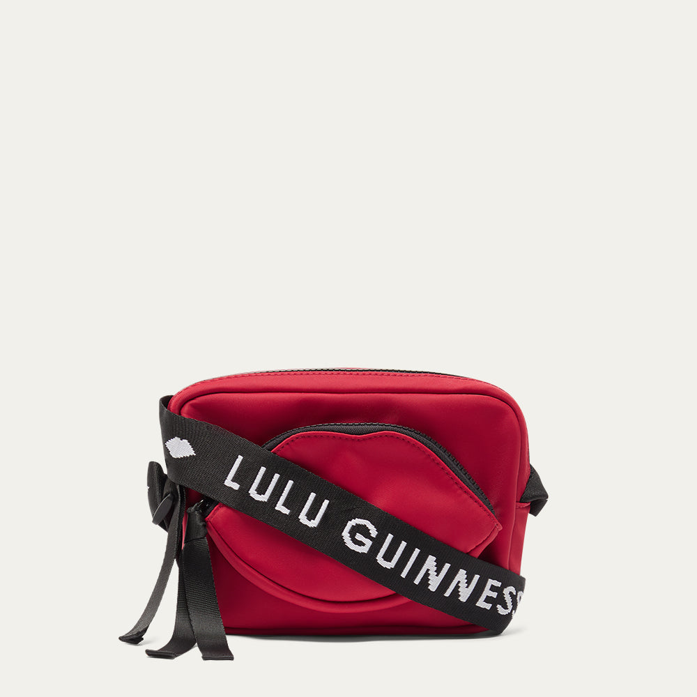 Red crossbody bag with a black strap featuring 'Lulu Guinness' on a light gray background