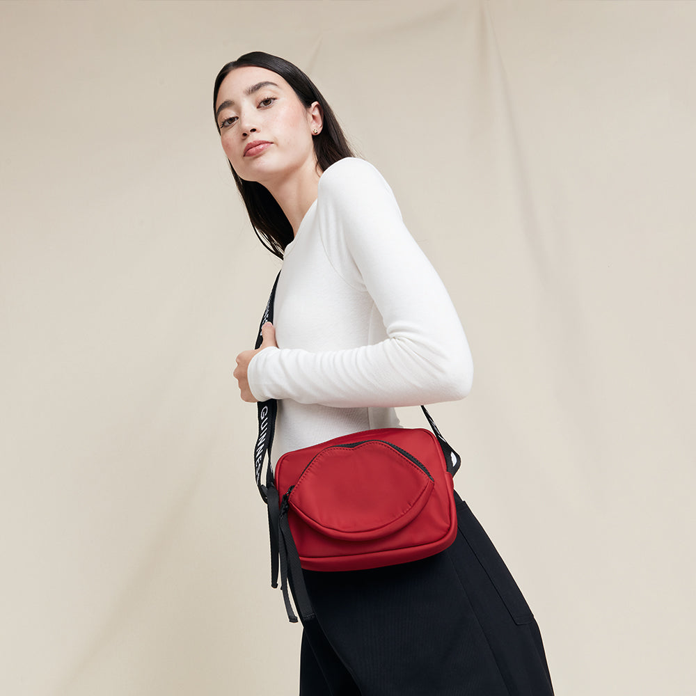 Woman carrying a red crossbody bag against a beige background
