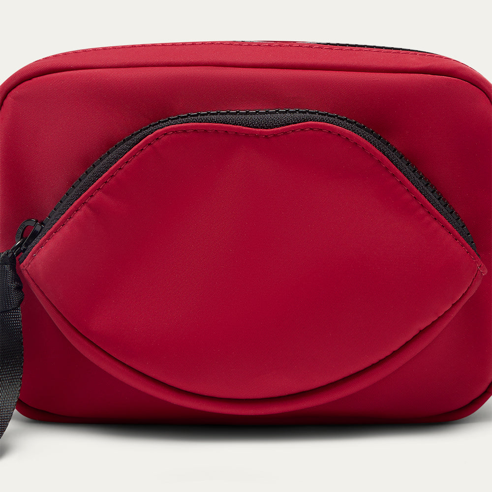 Close up image of a red crossbody bag with a lip-shaped pocket on a light gray background