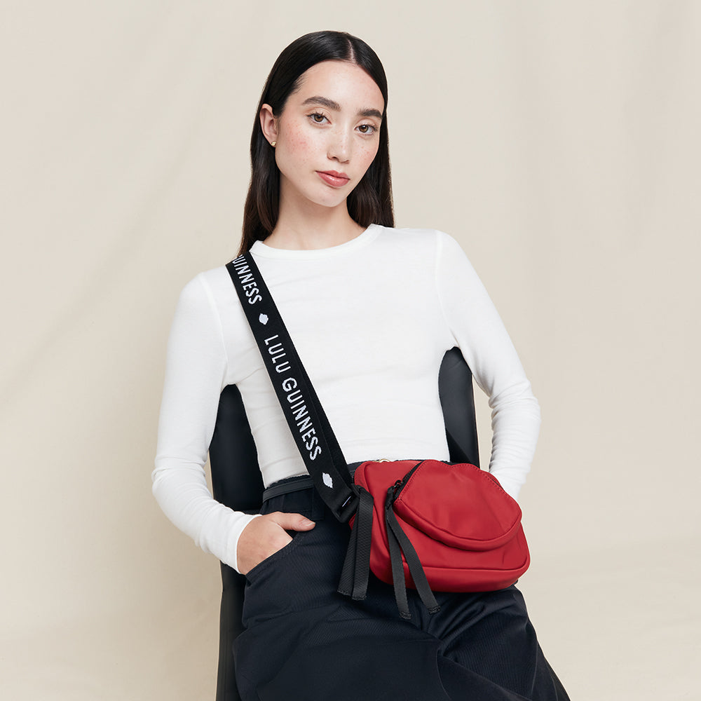 Woman wearing a red bag with 'Lulu Guinness' strap on a beige background