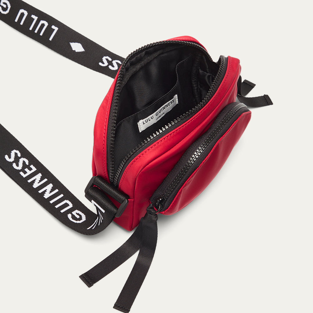 Red crossbody bag with black branded 'Lulu Guinness' strap open on a white background