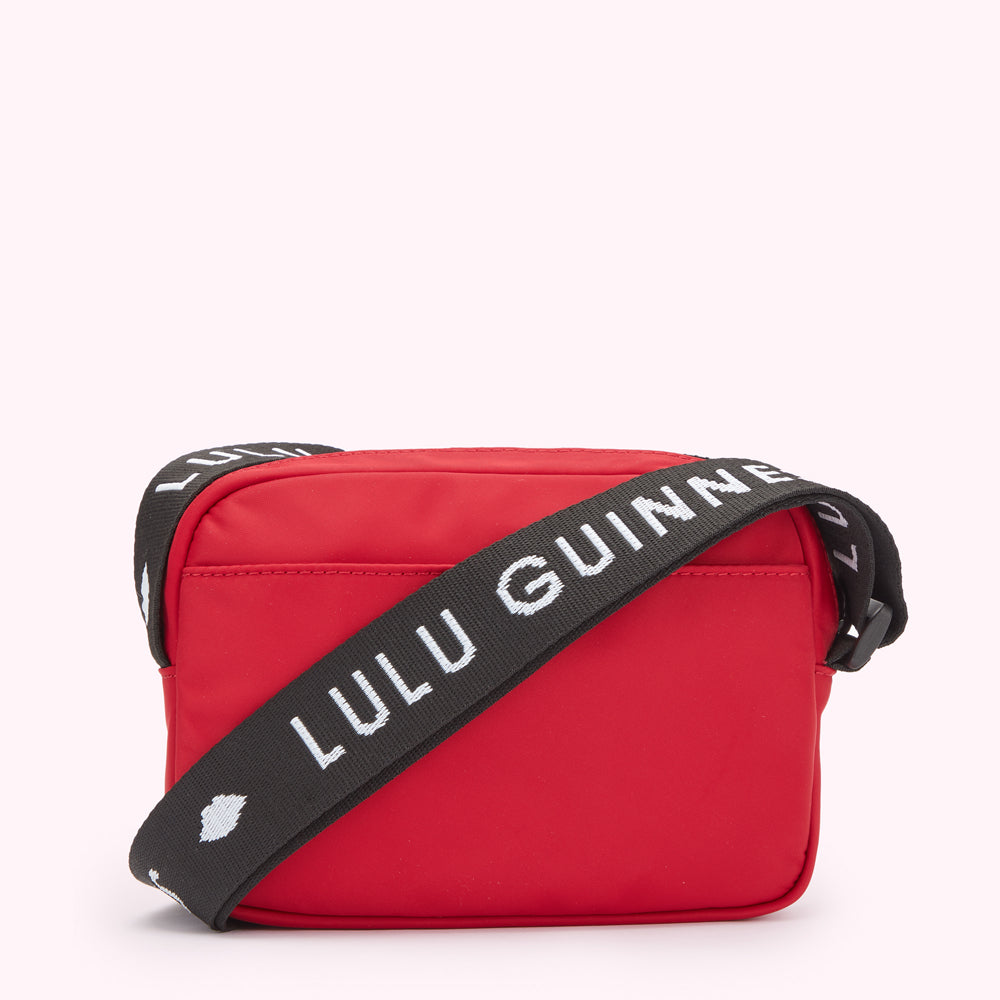 Red crossbody bag with black strap that says "Lulu Guinness" in white lettering.