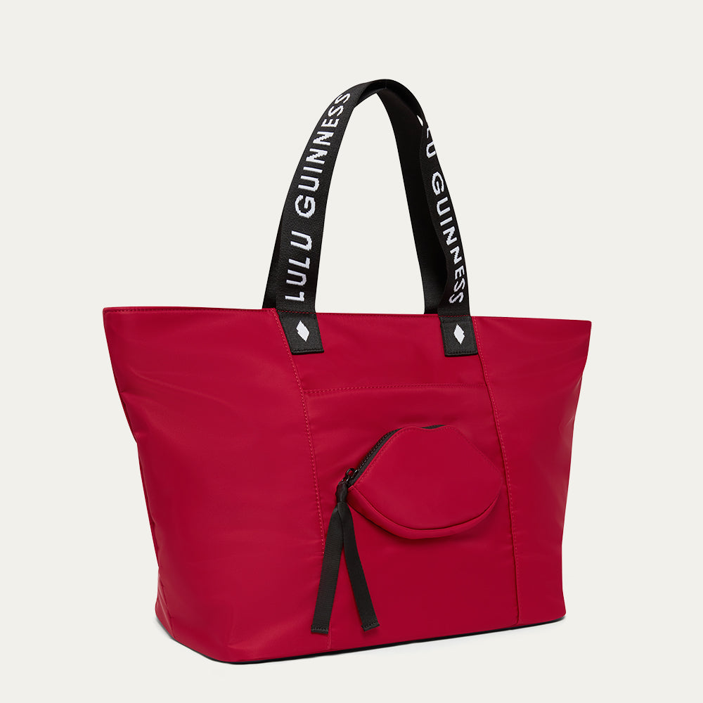 Red tote bag with black handles featuring 'Lulu Guinness' and a lip-shaped pocket on a light gray background